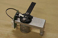 Photo of a microscope shutter. A black thin metal plate that can be moved to open or close the light path in a microscope.