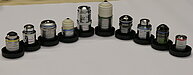 Photo of a series of microscope objectives of various types and designs. The objectives differ in magnification, size, and optical corrections, including achromatic, plan-achromatic, and apochromatic types. Some objectives are finite-corrected, others infinite-corrected. The photo illustrates the diverse components used for producing magnified images in light microscopy, highlighting the complexity and specialization of microscope optics