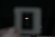 This image shows a mostly black background with several bright points of white light near the center. The light sources are very close to each other, and each emits several thin, straight lines spreading horizontally, which makes a star-like effect. Around these lines, there are faint colored strips—mainly green and red—which create a subtle rainbow effect extending from the bright points. The rest of the image is dark, and the lights stand out sharply in the center.